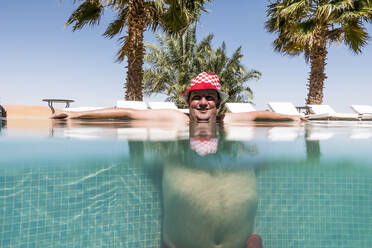 Overweight man with hat bathing in pool - OCMF00790