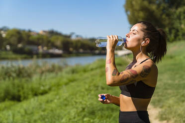 Sportliche junge Frau bei einer Abkühlungspause am Flussufer - MGIF00750