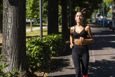 Portrait of young woman running on a tree-lined road - MGIF00752