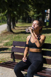 Sportliche junge Frau macht eine Abkühlungspause auf einer Parkbank - MGIF00757
