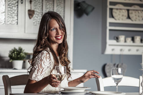 Porträt einer lächelnden jungen Frau, die an einem gedeckten Tisch in einer Küche im Landhausstil sitzt - WFF00108