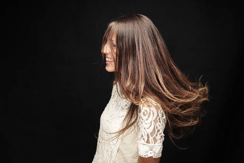 Glückliche junge Frau mit langen braunen Haaren vor schwarzem Hintergrund, lizenzfreies Stockfoto