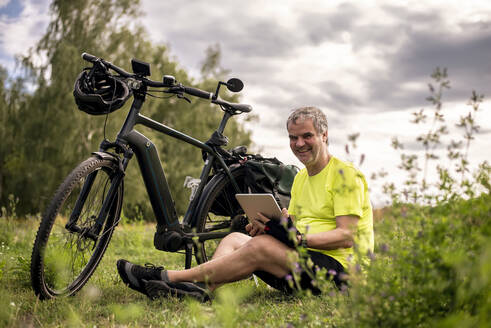 Happy mature man using digital tablet during his bike tour with an e-bike - BFRF02095
