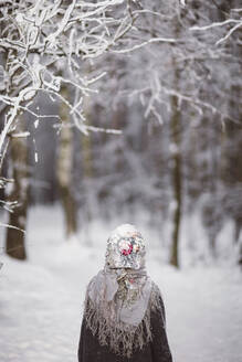 Rückenansicht eines kleinen Mädchens mit Kopftuch, das vor einem Winterwald steht - EYAF00495