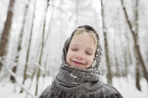 Porträt eines glücklichen kleinen Mädchens mit Kopftuch im Winterwald, lizenzfreies Stockfoto