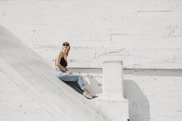 Young woman sitting in front of a white wall outdoors - LHPF01000