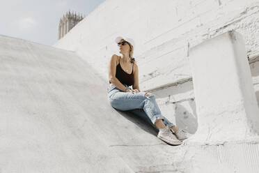 Young woman sitting in front of a white wall outdoors - LHPF01001