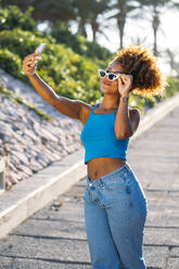 Porträt einer jungen Frau mit Sonnenbrille, die ein Selfie mit ihrem Smartphone macht - MPPF00057