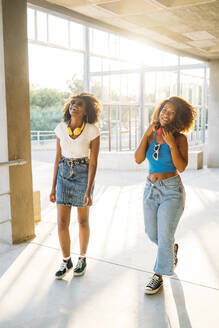 Portrait of two laughing young women with headphones during sunset - MPPF00078