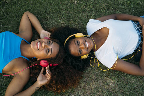 Portrait of two happy young women lying on meadow listening music with headphones - MPPF00087