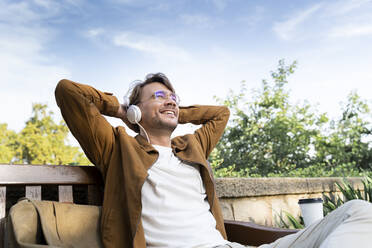 Laughing man sitting on bench listening music with headphones - AFVF04032