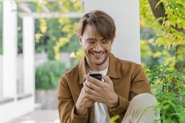 Porträt eines lachenden Mannes, der auf sein Handy schaut - AFVF04042