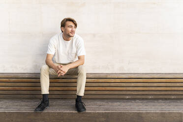 Portrait of man sitting on wooden bench looking at distance - AFVF04049