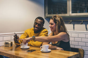 Porträt eines lächelnden Paares in einem Café mit Smartphone - CJMF00041