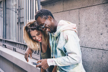 Lachendes Paar, das im Freien ein Mobiltelefon benutzt - CJMF00047
