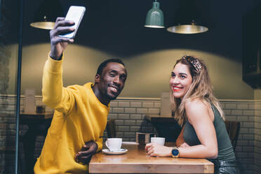 Porträt eines lächelnden Paares in einem Café, das ein Selfie mit seinem Smartphone macht - CJMF00049