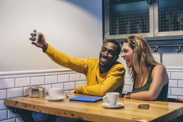 Porträt eines lachenden Paares, das in einem Café ein Selfie mit seinem Smartphone macht - CJMF00055