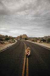 Frau sitzt auf der Straße, Joshua Tree National Park, Kalifornien, USA - LHPF01012