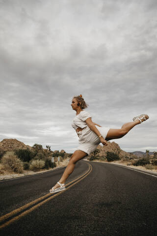 Frau springt auf Straße, Joshua Tree National Park, Kalifornien, USA, lizenzfreies Stockfoto