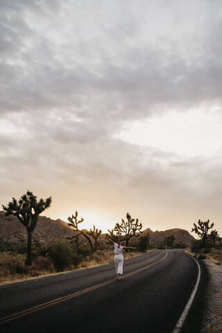 Frau geht bei Sonnenuntergang auf der Straße, Joshua Tree National Park, Kalifornien, USA, lizenzfreies Stockfoto