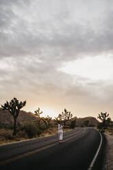 Frau geht bei Sonnenuntergang auf der Straße, Joshua Tree National Park, Kalifornien, USA - LHPF01023
