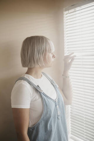Junge Frau blickt durch die Jalousien auf das Fenster, lizenzfreies Stockfoto