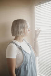 Young woman looking through blinds at the window - LHPF01032