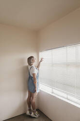 Junge Frau blickt durch die Jalousien auf das Fenster - LHPF01036