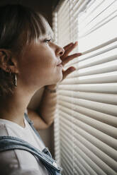 Young woman looking through blinds at the window - LHPF01037