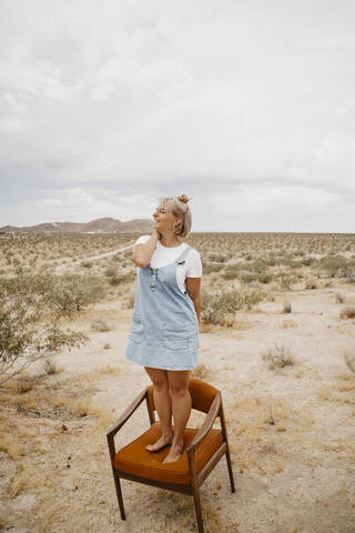 Frau auf einem Stuhl stehend in Wüstenlandschaft, Joshua Tree National Park, Kalifornien, USA, lizenzfreies Stockfoto