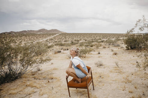 Frau hockt auf einem Stuhl in Wüstenlandschaft, Joshua Tree National Park, Kalifornien, USA - LHPF01049