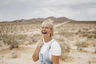 Porträt einer lachenden jungen Frau in einer Wüstenlandschaft, Joshua Tree National Park, Kalifornien, USA - LHPF01053