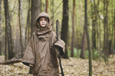 Portrait of boy wearing brown rain coat standing in autumnal forest - EYAF00511