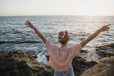 Rückansicht einer jungen Frau am Meer mit erhobenen Armen, Sunset Cliffs, San Diego, Kalifornien, USA - LHPF01067