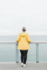 Rear view of young woman wearing yellow rain coat - NAF00124