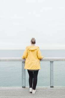 Rückansicht einer jungen Frau mit gelbem Regenmantel - NAF00124