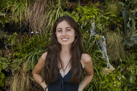 Porträt einer lächelnden jungen Frau vor einer Pflanzenwand, lizenzfreies Stockfoto
