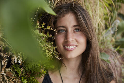 Porträt einer lächelnden jungen Frau vor einer Pflanzenwand, lizenzfreies Stockfoto