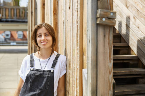 Porträt einer lächelnden jungen Frau, die sich an einen Holzzaun lehnt - SUF00607