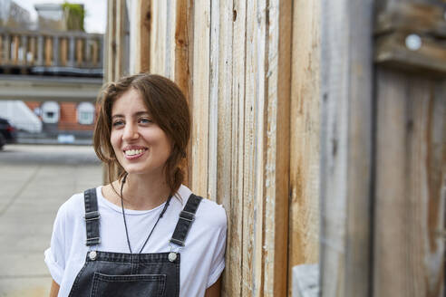 Portrait of smiling young woman leaning agianst wooden fence - SUF00608