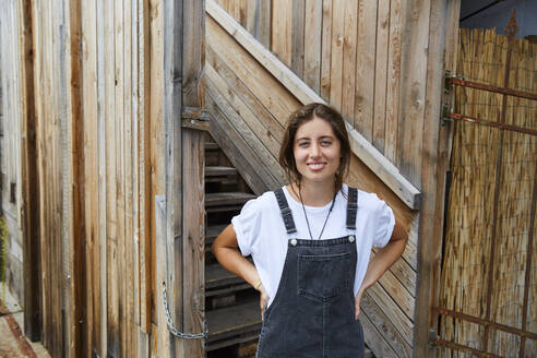 Portrait of smiling young woman in front of wooden fence - SUF00609