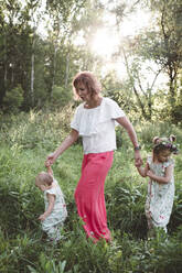 Mutter mit zwei Töchtern beim Spaziergang auf einer Wiese - EYAF00515