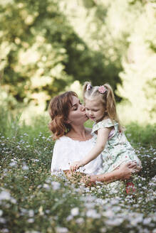 Mutter küsst ihre Tochter auf einer Blumenwiese - EYAF00518