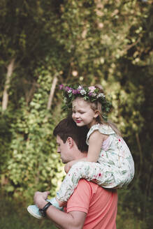 Father carrying daughter with flower wreath on his shoulders - EYAF00523