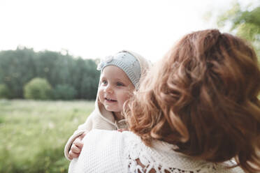 Happy little girl looking over mother's shoulder - EYAF00537