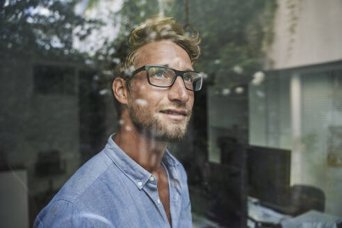 Lässiger junger Geschäftsmann hinter einer Fensterscheibe im Büro - PNEF02079