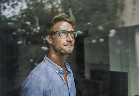 Casual young businessman behind windowpane in office - PNEF02080