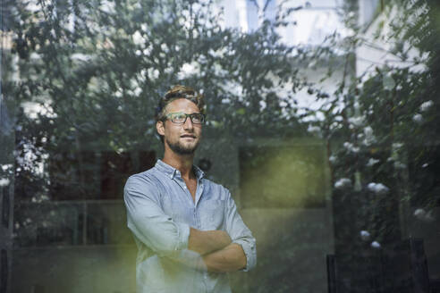 Lässiger junger Geschäftsmann hinter einer Fensterscheibe im Büro - PNEF02082