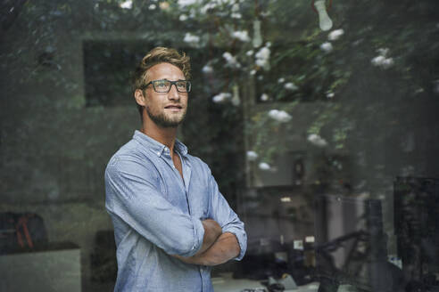 Casual young businessman behind windowpane in office - PNEF02083