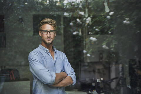 Porträt eines lässigen jungen Geschäftsmannes hinter einer Fensterscheibe im Büro, lizenzfreies Stockfoto